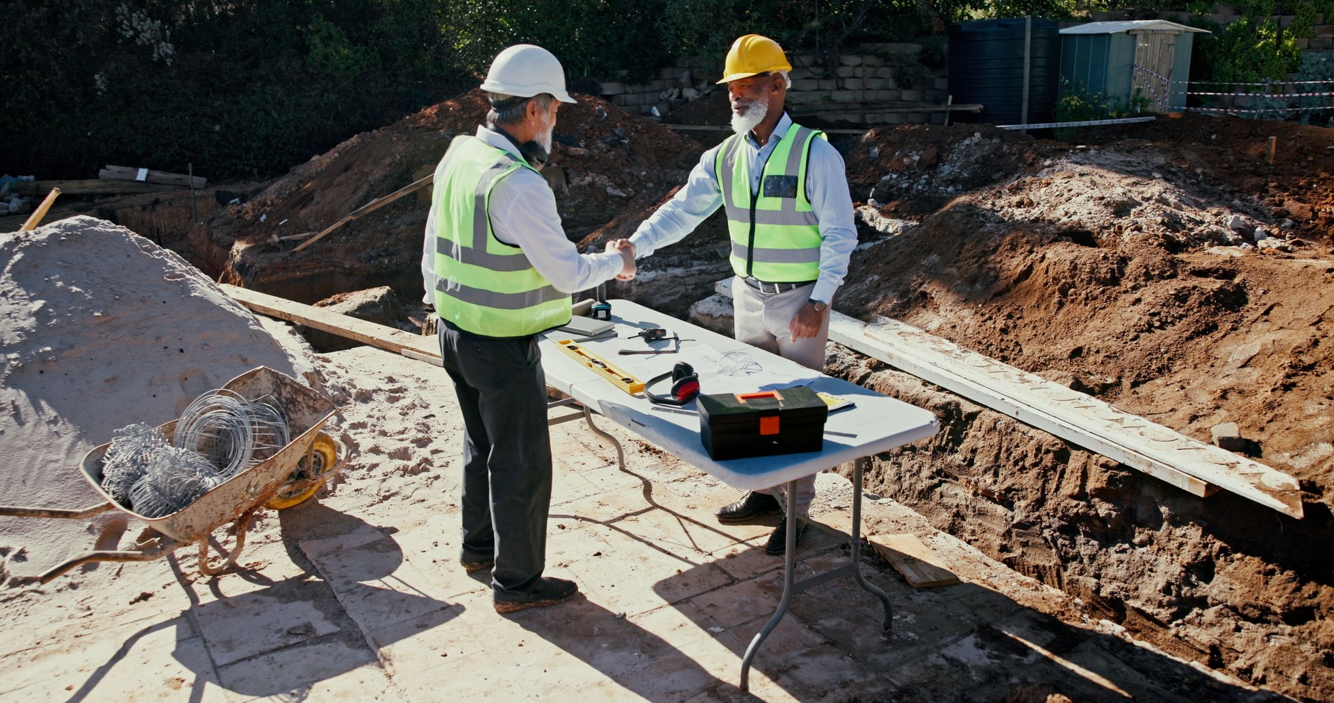 Construction worker, handshake and engineer people in partnership outdoor to start foundation. Mature men, foreman or employees with deal for excavation, agreement or collaboration and shaking hands